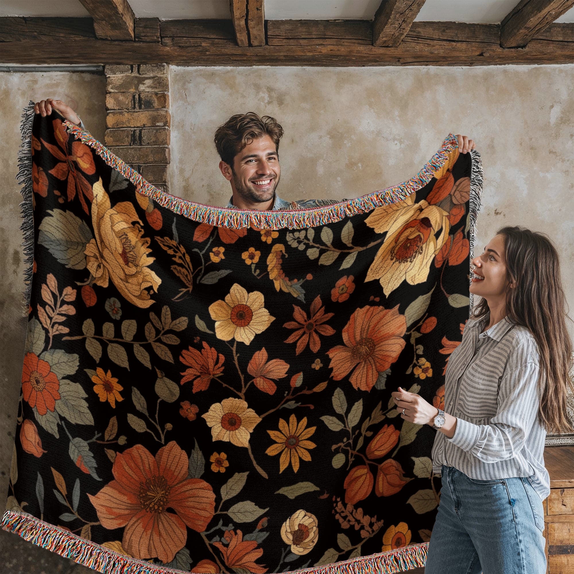 Two people holding up a floral blanket with autumn colors in a rustic room.