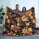 Two people holding a floral and pumpkin patterned blanket indoors.