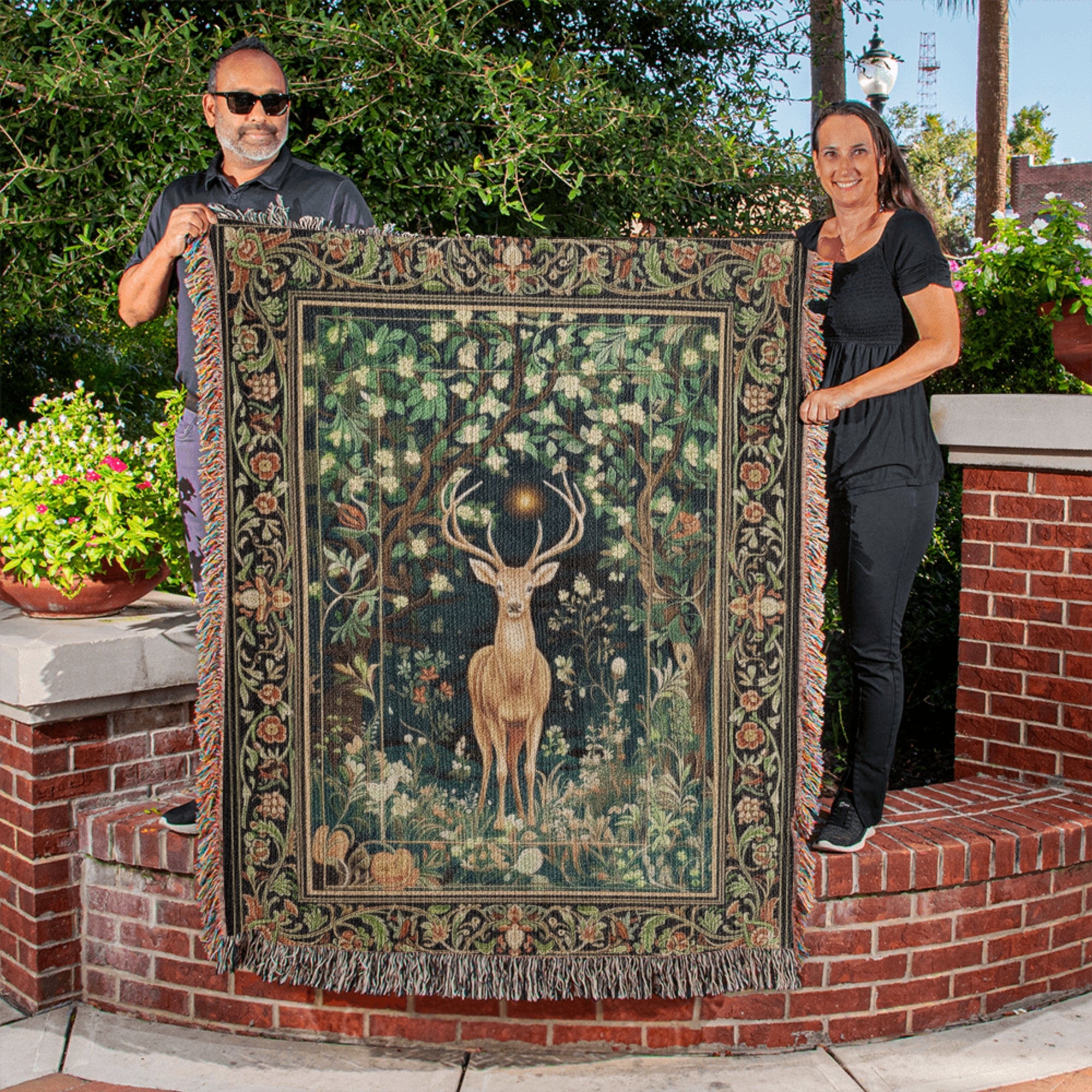 Two people holding a large tapestry with a deer design outdoors.